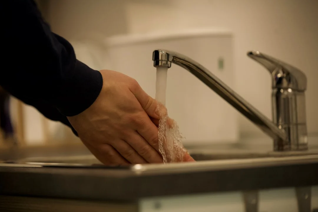 Gloved hands cleaning cabinet handles with a spray bottle and cloth for hygiene.